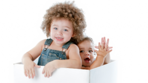 two smiling toddler playing in a white box