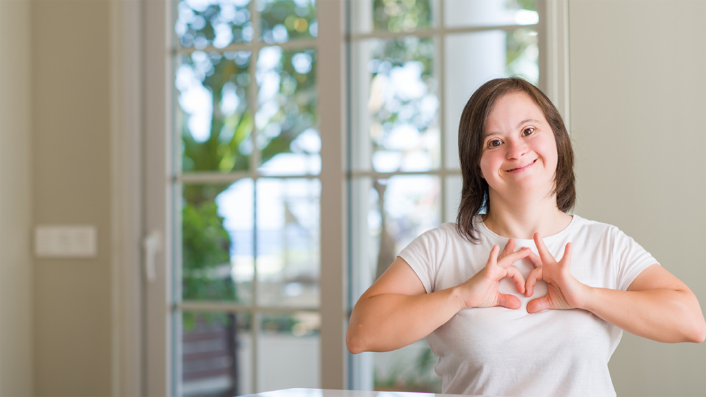 Smiling young woman with Down syndrome making a heart sign with her hands