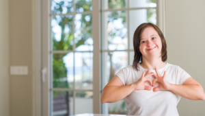 Smiling young woman with Down syndrome making a heart sign with her hands