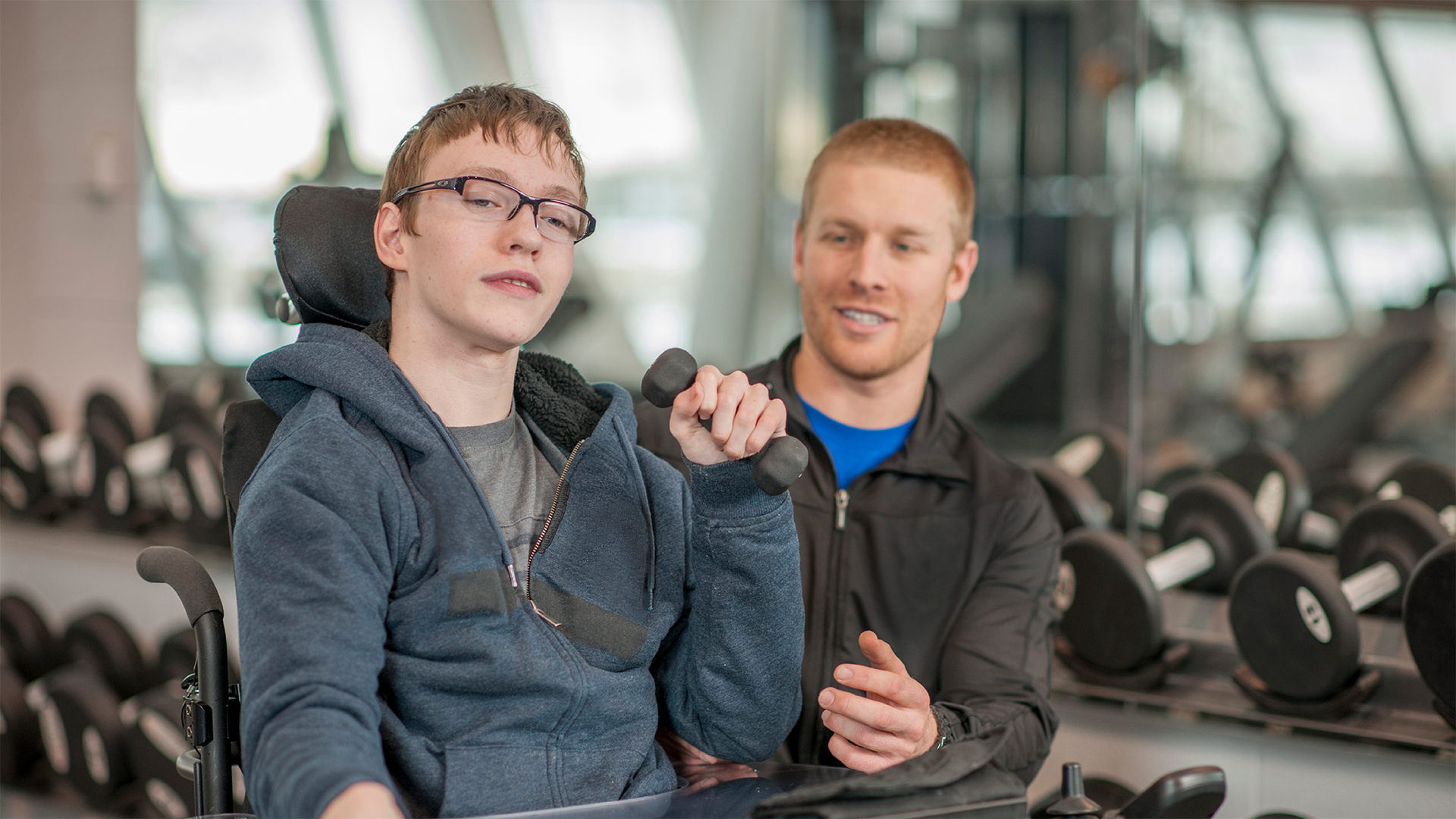 Young man in wheelchair assisted by therapist