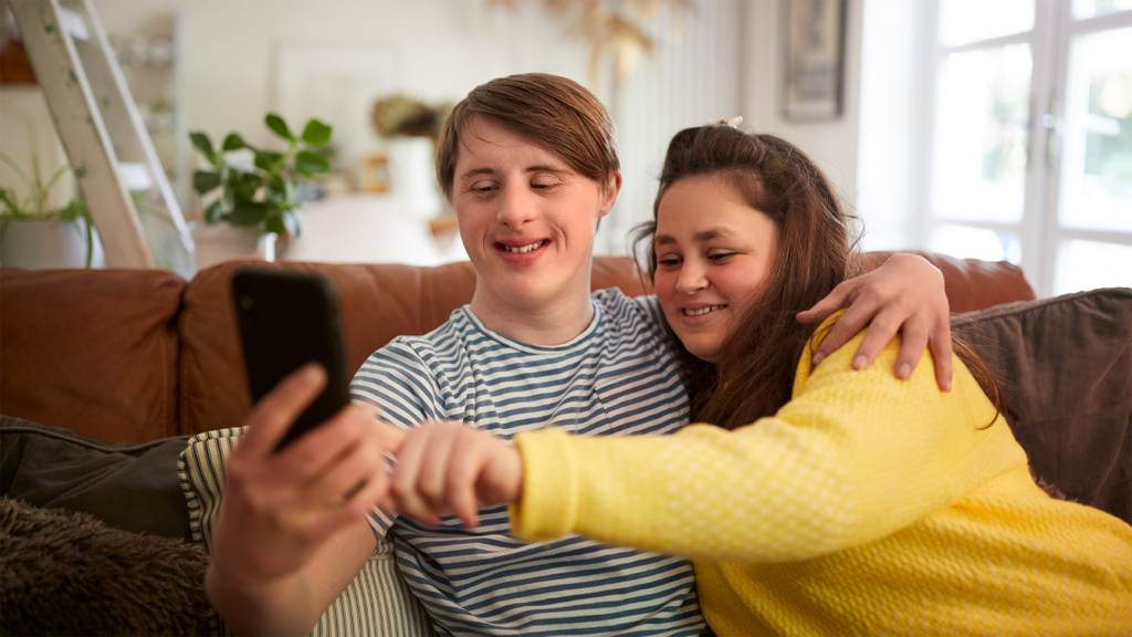 Young couple with Down syndrome sitting on sofa taking a selfie