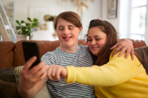 Young couple with Down syndrome sitting on sofa taking a selfie