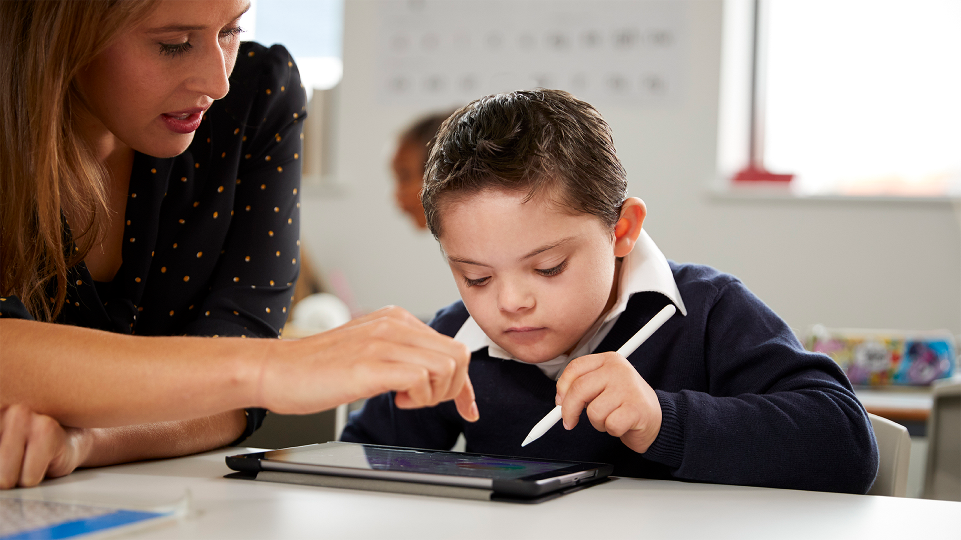 Teacher helping young boy with Down syndrome use tablet