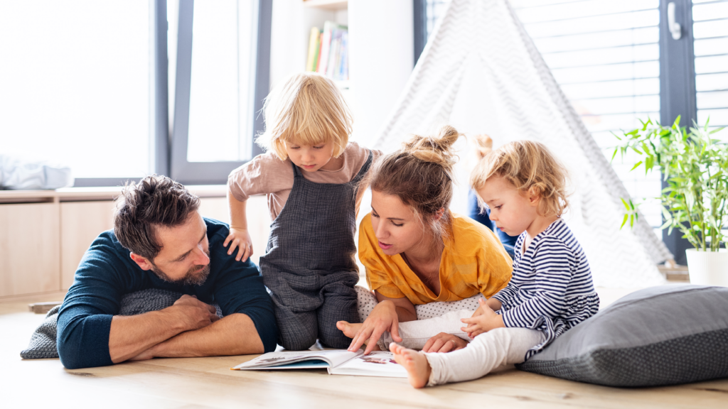 Family with two children on floor looking at a book together