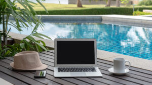 laptop and coffee cup on a table next to a pool