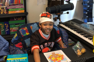 Young smiling boy in his room surrounded by books toys keyboard telescope