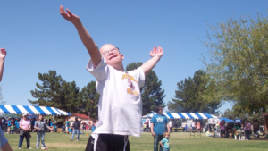 young man with Down syndrome with arms lifted and smiling at the sky