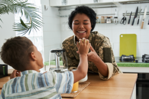 smiling woman in military uniform holding the hand of a young boy sitting across the table from her