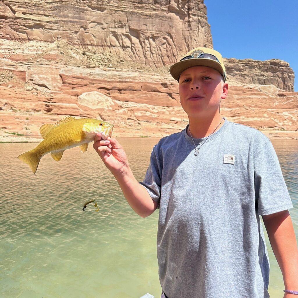 young boy holding a yello fish he just caught in an Arizona lake with a beautiful butte in the background.