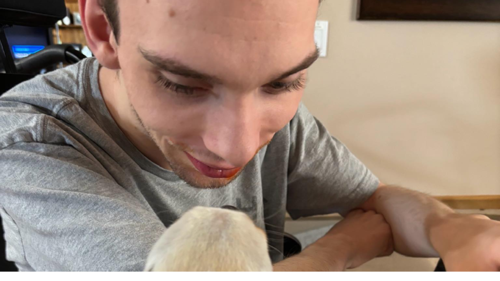 Young man sitting in his wheelchair looking down at his dog